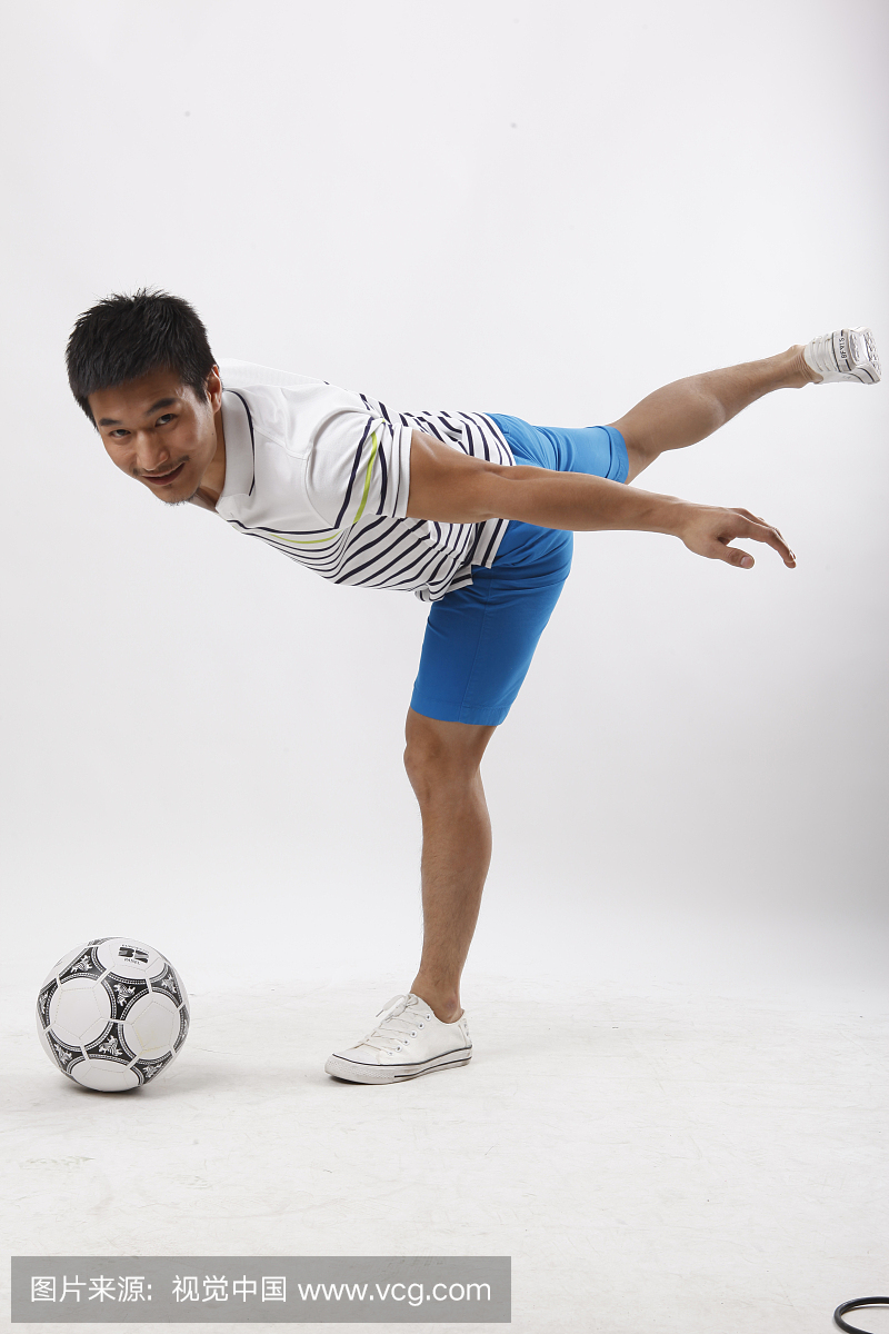 一个穿休闲装踢足球的青年男士