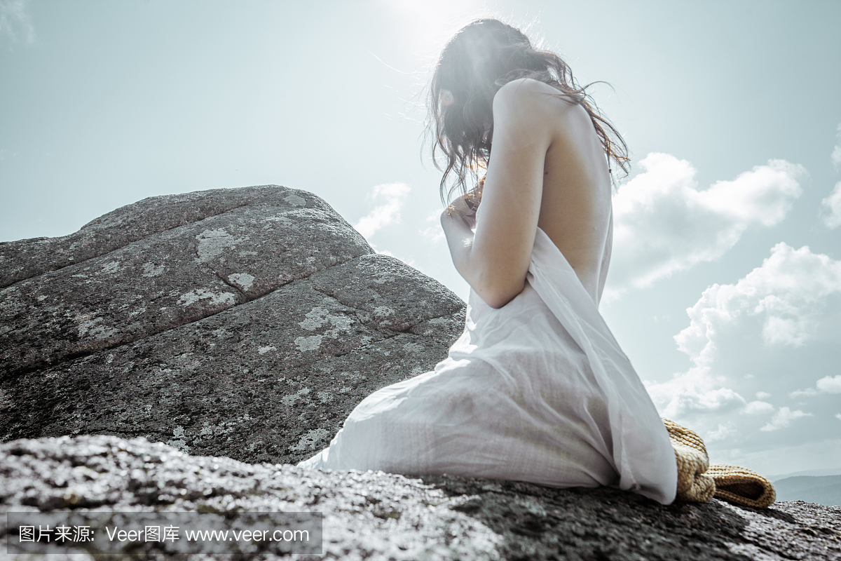 白色长布裙下的女孩在夏天的大石头上非常高