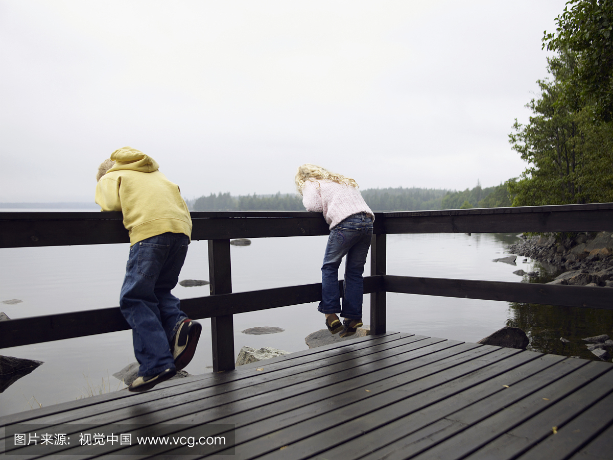 年轻的男孩和女孩靠在湖边的栏杆上。