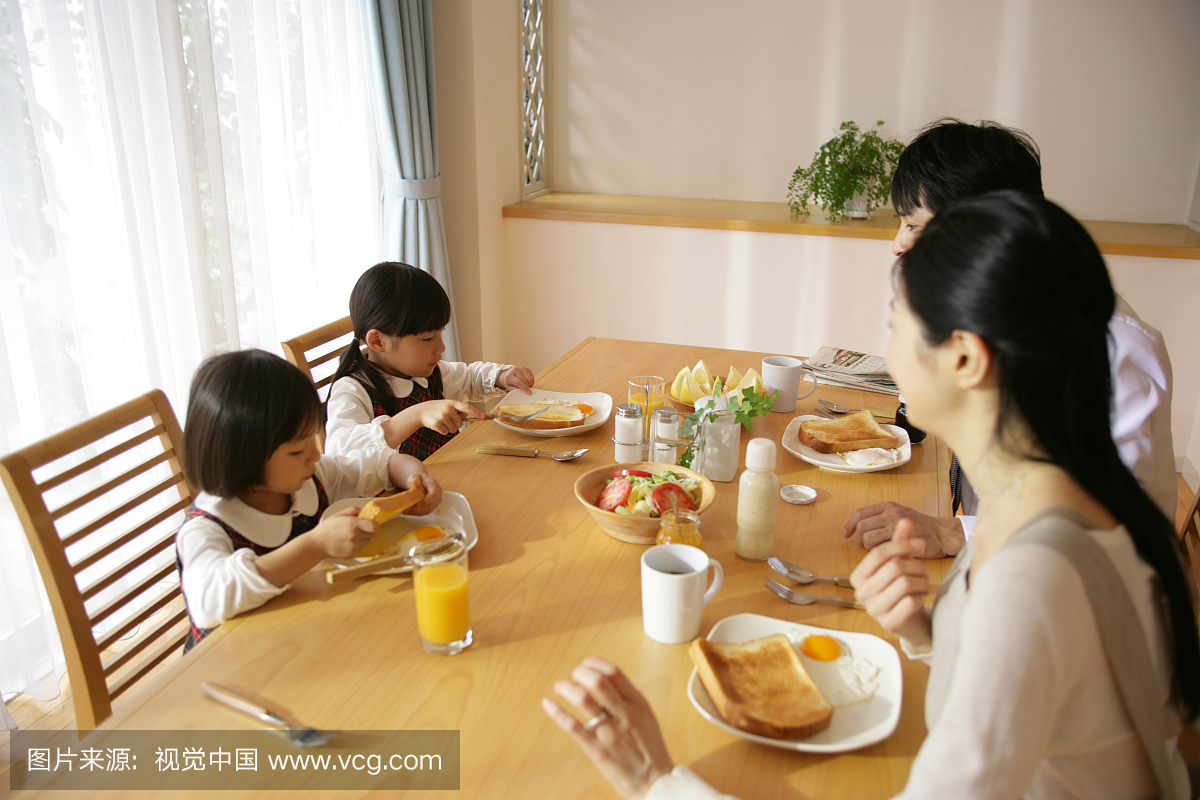 中间成年夫妇和他们的女儿坐在餐桌上的高角度