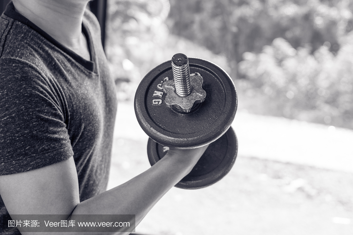 男人手举钢钢哑铃在健身房肌肉建设黑白图像,
