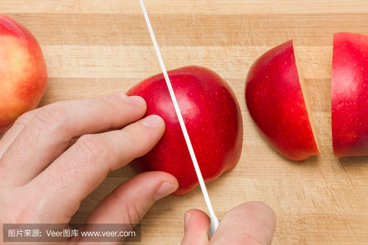 厨师的双手用刀在木板上切割红苹果,以便在厨