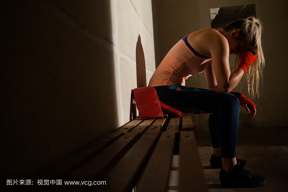 Sad woman sitting on bench in fitness studio