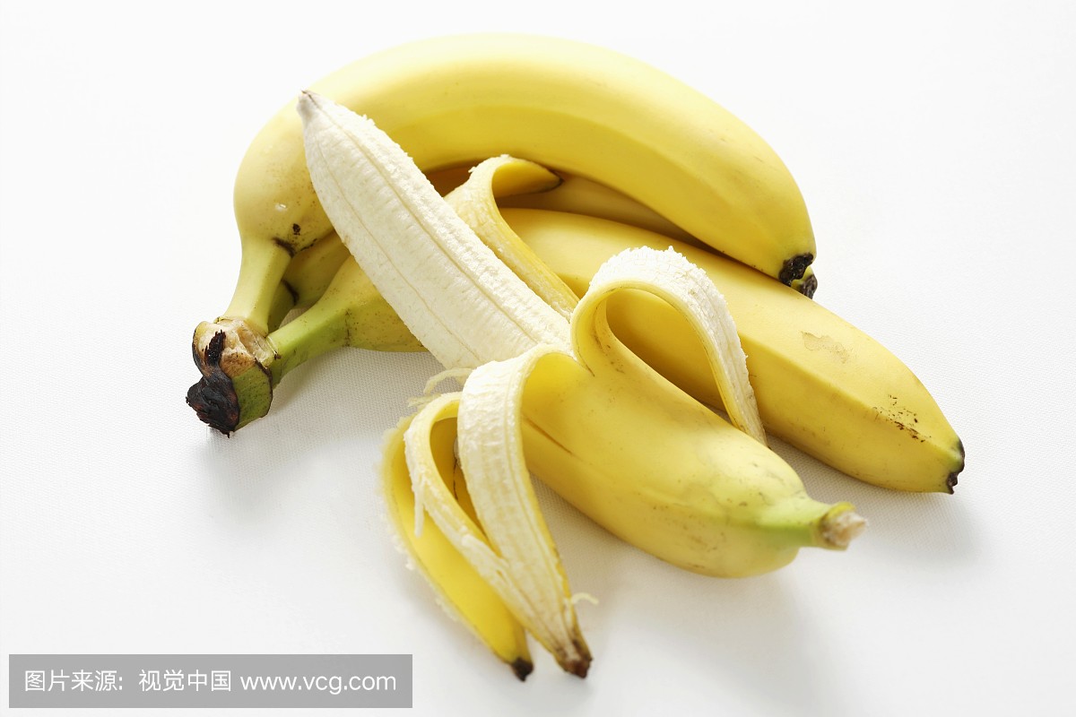 Half-peeled banana in front of small bunch of ba