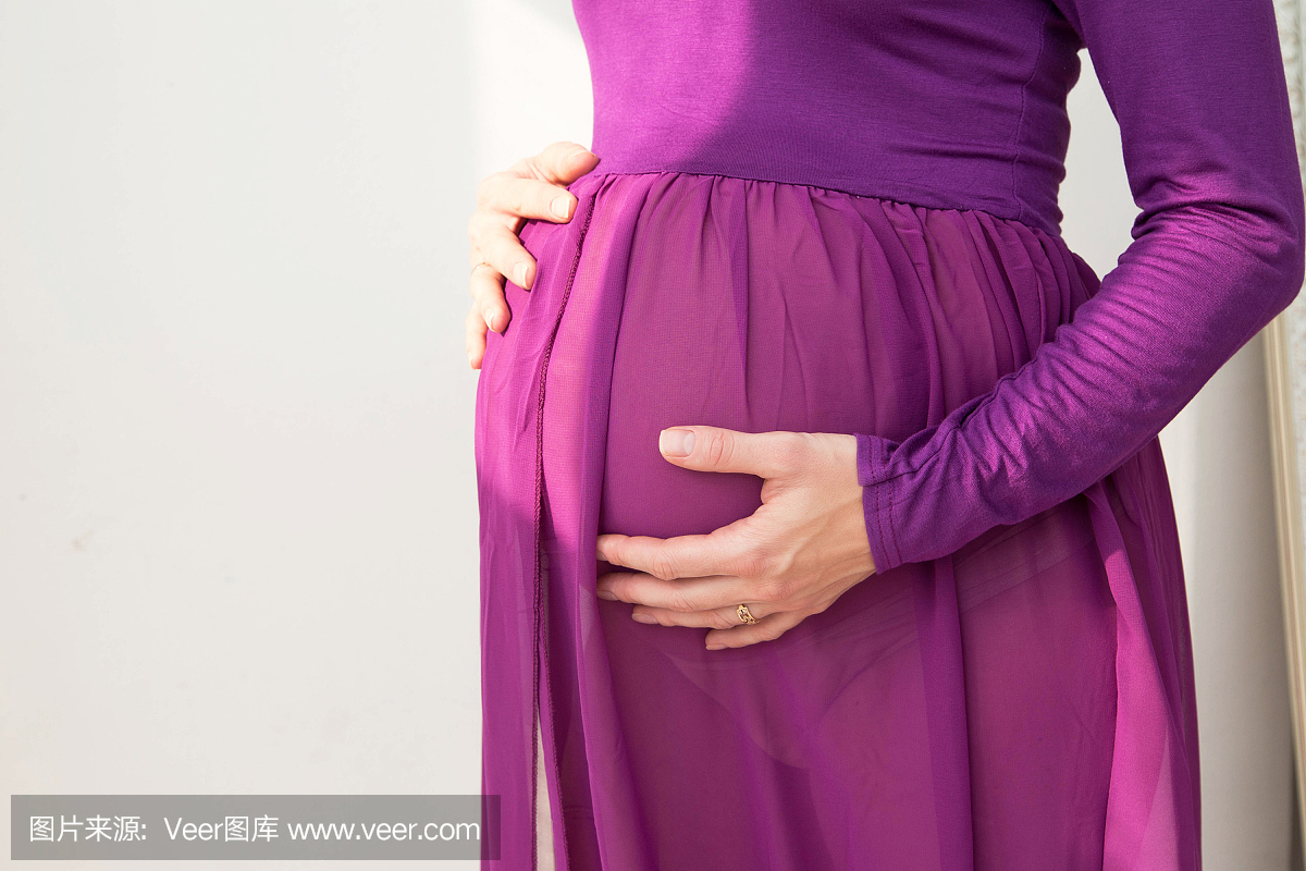 穿着紫色衣服的孕妇把她的手放在她的肚子上