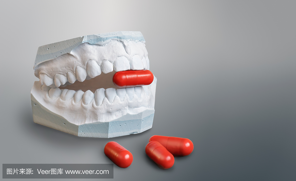 拿着红色医学胶囊的石膏牙模型