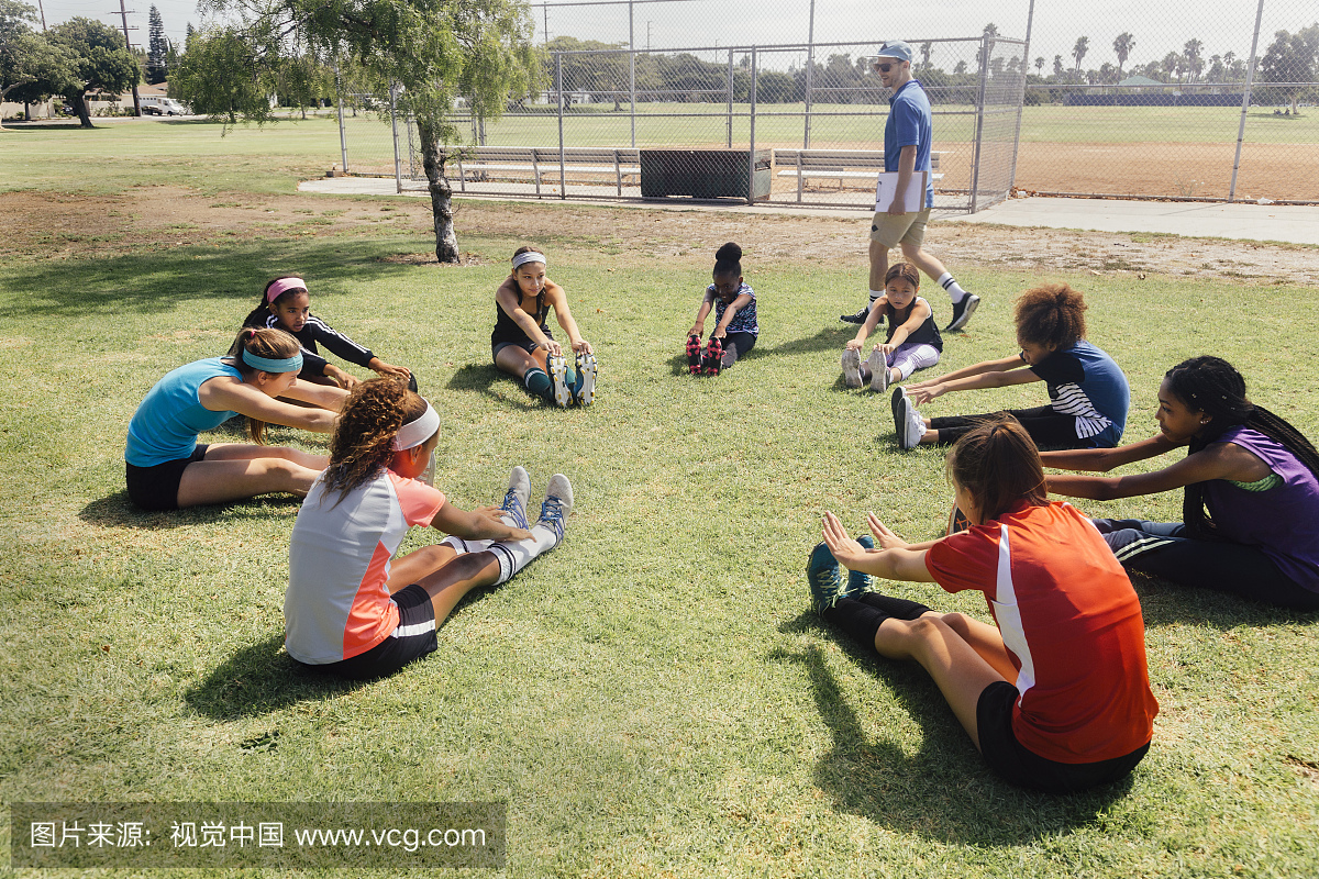 老师指导女学生足球运动员在学校运动场热身