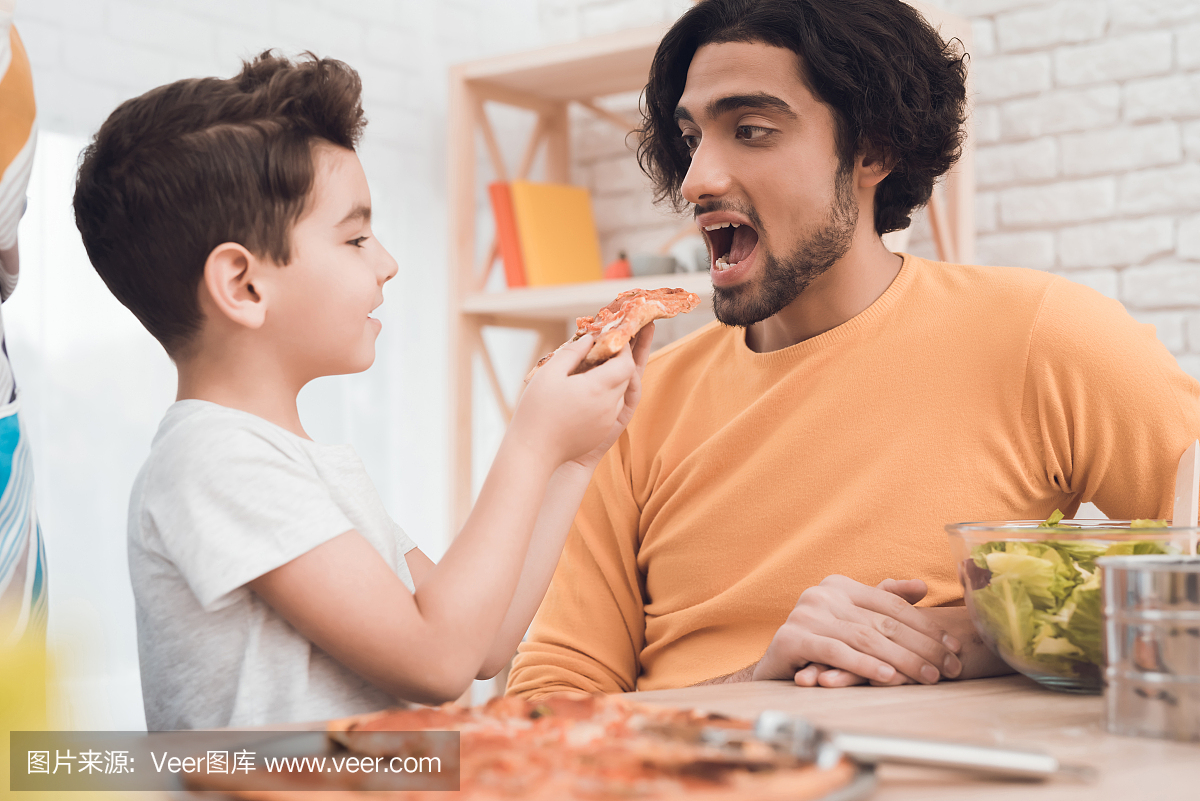 一个小男孩和他的阿拉伯父亲一起吃披萨。
