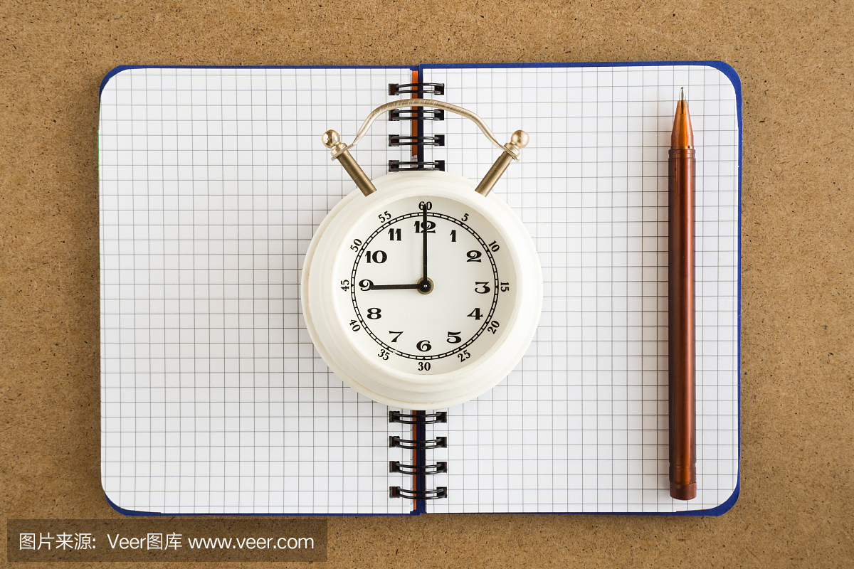 笔记本用钢笔和木制的桌子上的时钟。时间不多