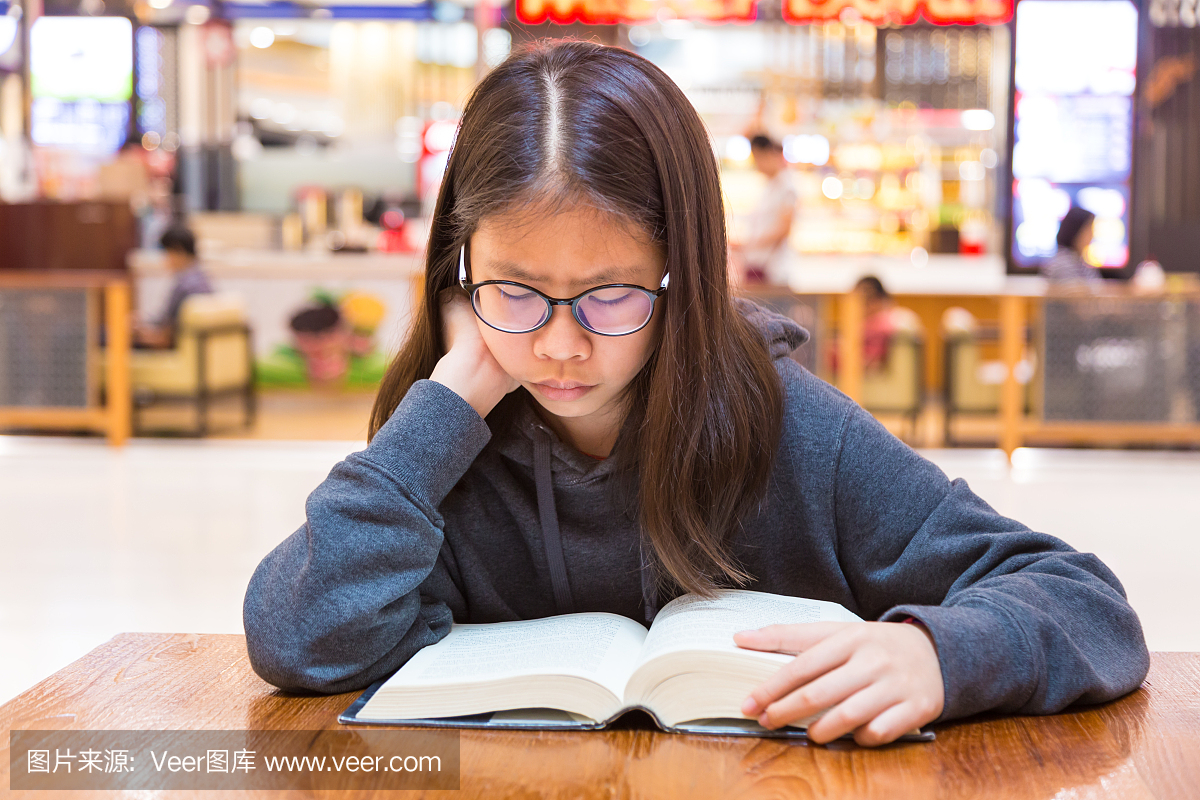 戴眼镜的女孩读一本厚实的小说故事书在一个公