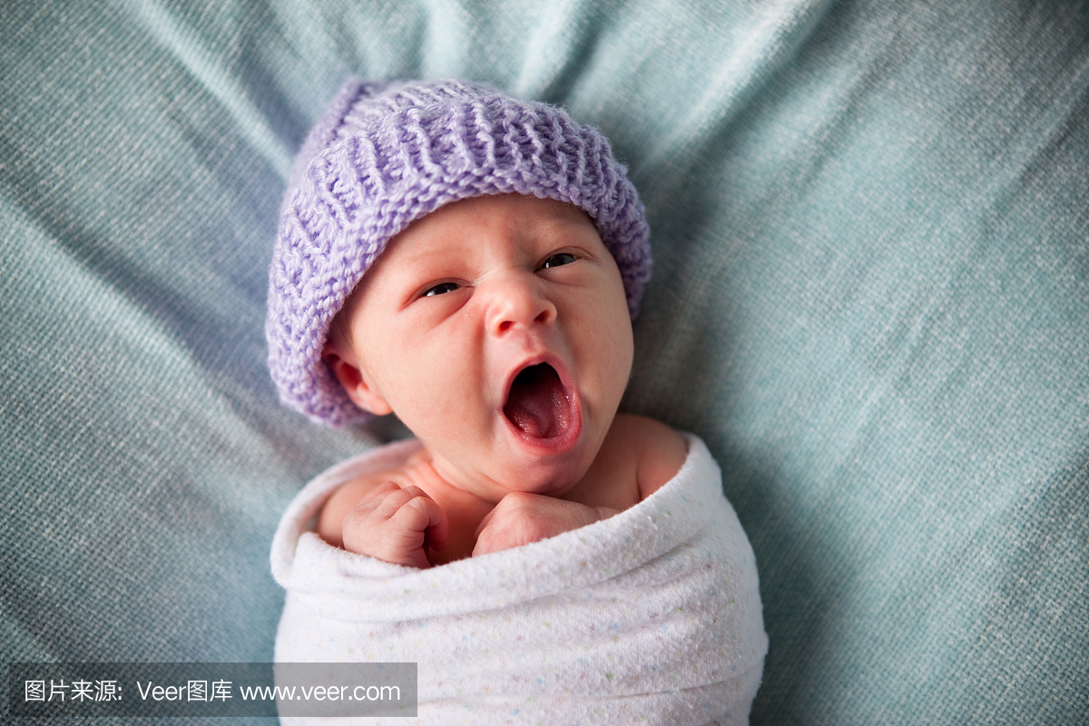 疲惫的新生婴儿打呵欠,被包裹在毯子里