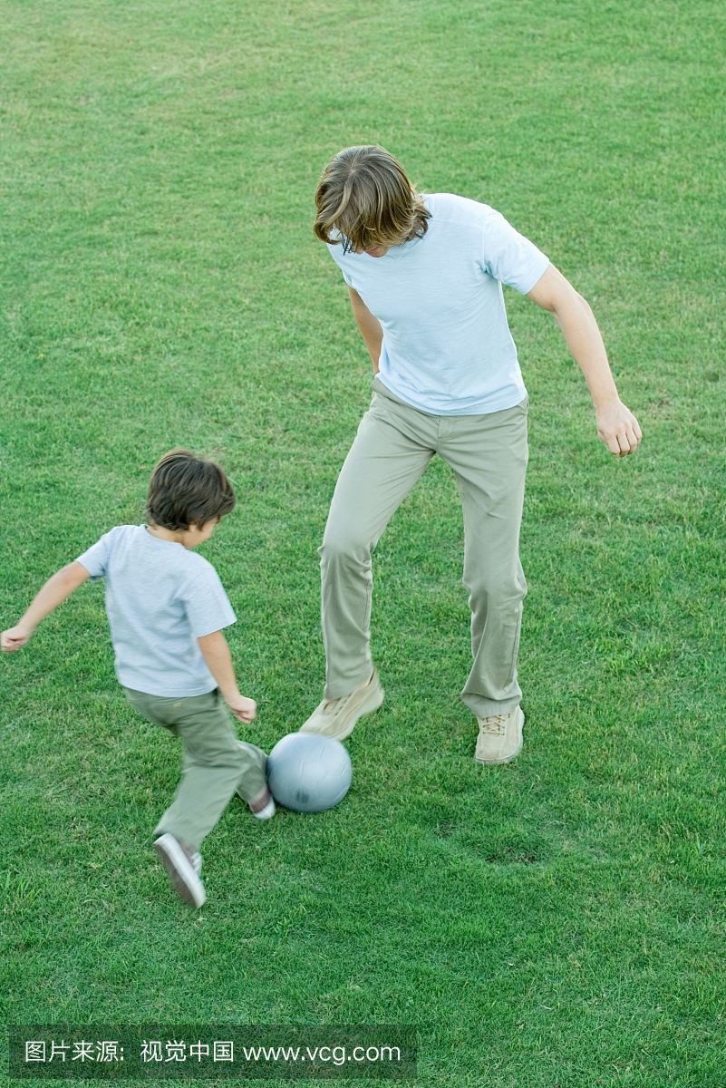 年轻男子和男孩在草坪上踢足球,高角度视图