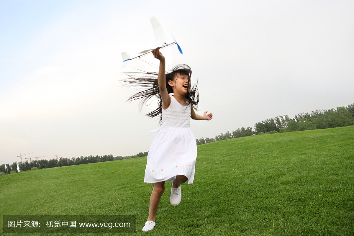 一个东方女孩在草上玩飞机模型