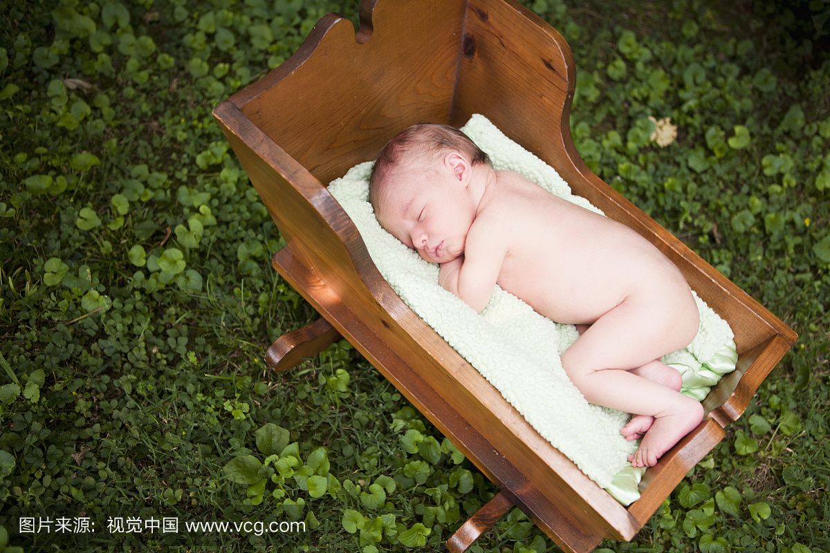 一个裸体的新生婴儿睡在一个木制的摇篮里