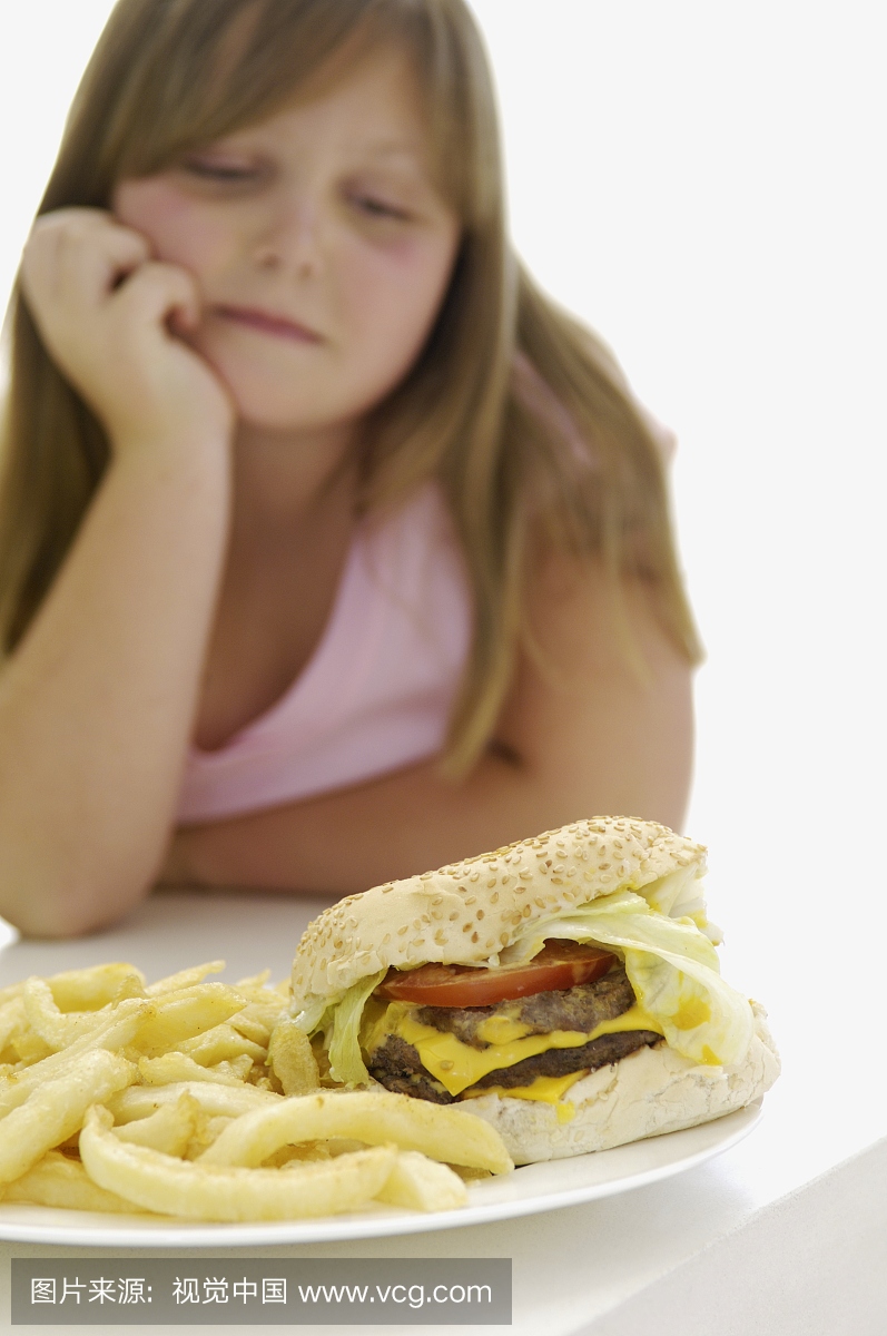 超重的女孩看着汉堡包和炸薯条