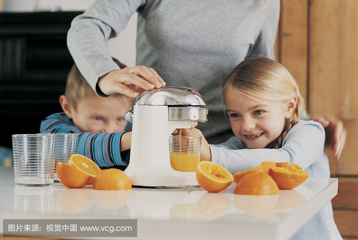 母亲制作橙汁在厨房使用榨汁机与她的儿子和女
