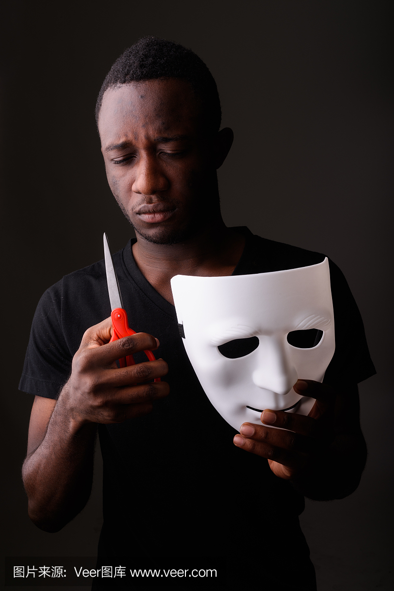 工作室拍摄的年轻黑人非洲男子拿着面具和剪刀