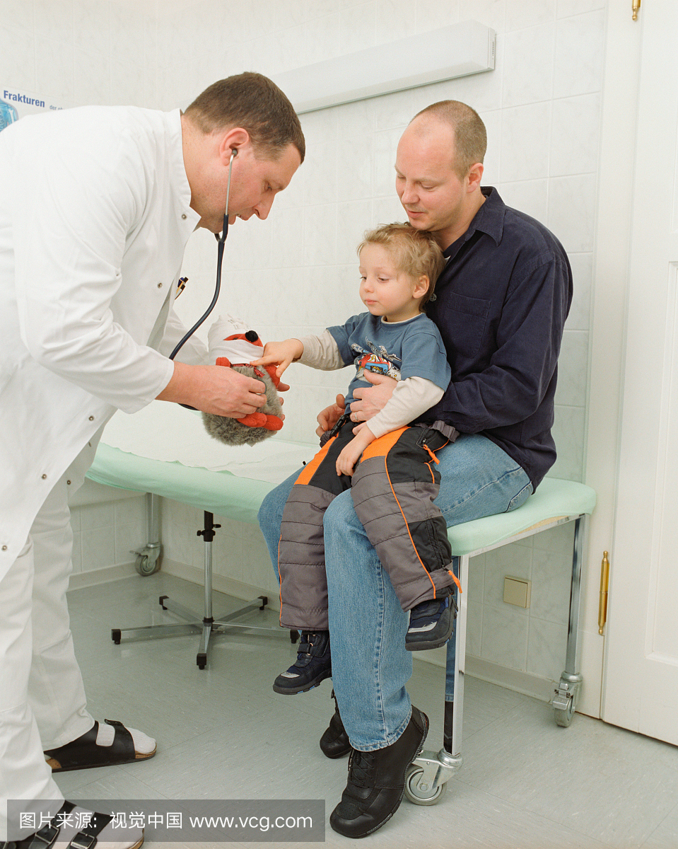 医生在父亲的膝盖上向男孩(2-4)展示毛绒玩具