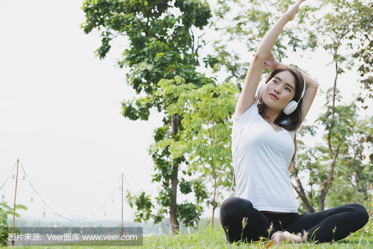 亚洲孕妇练习瑜伽,同时在公园的绿草上听音乐