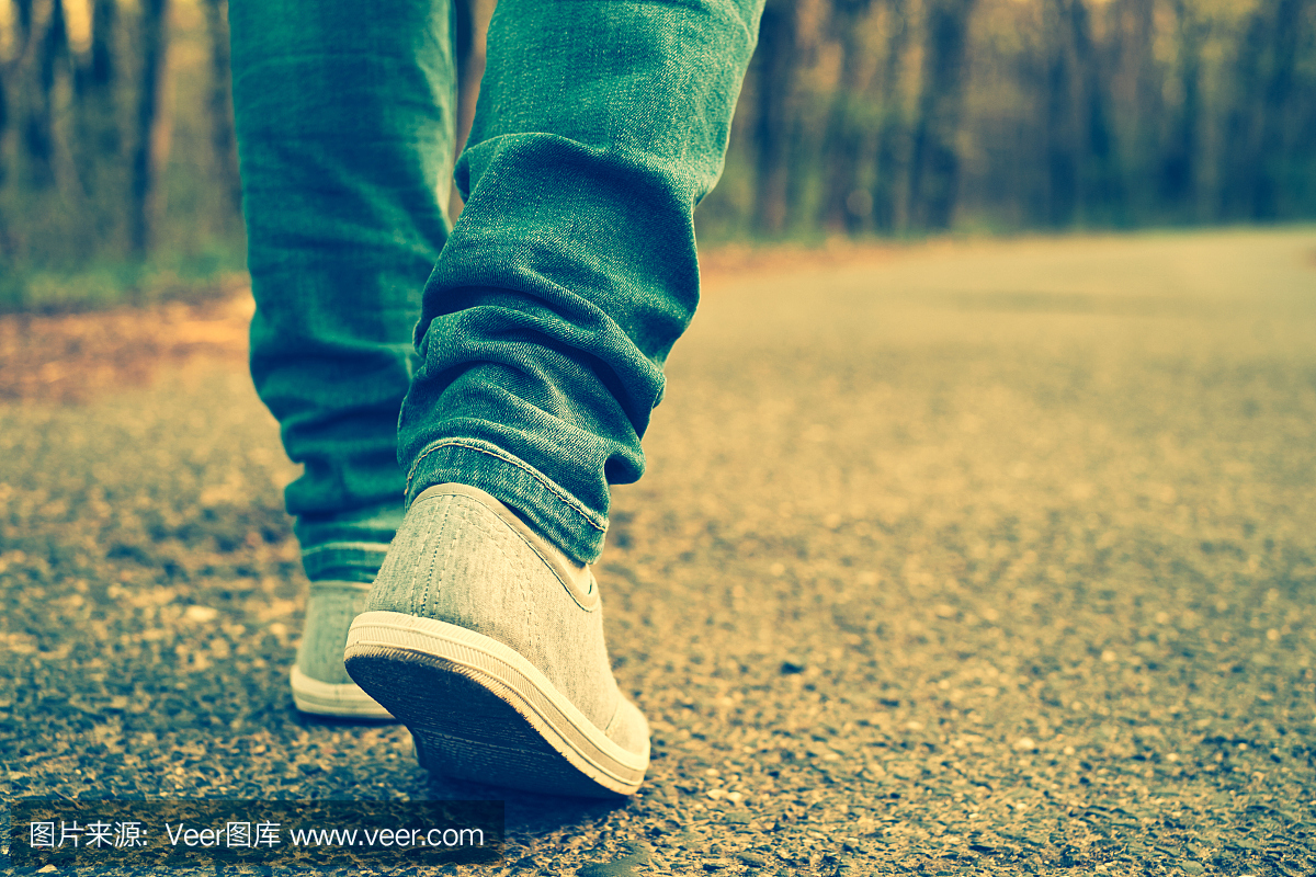 有人在路上独自走路的牛仔裤和运动鞋