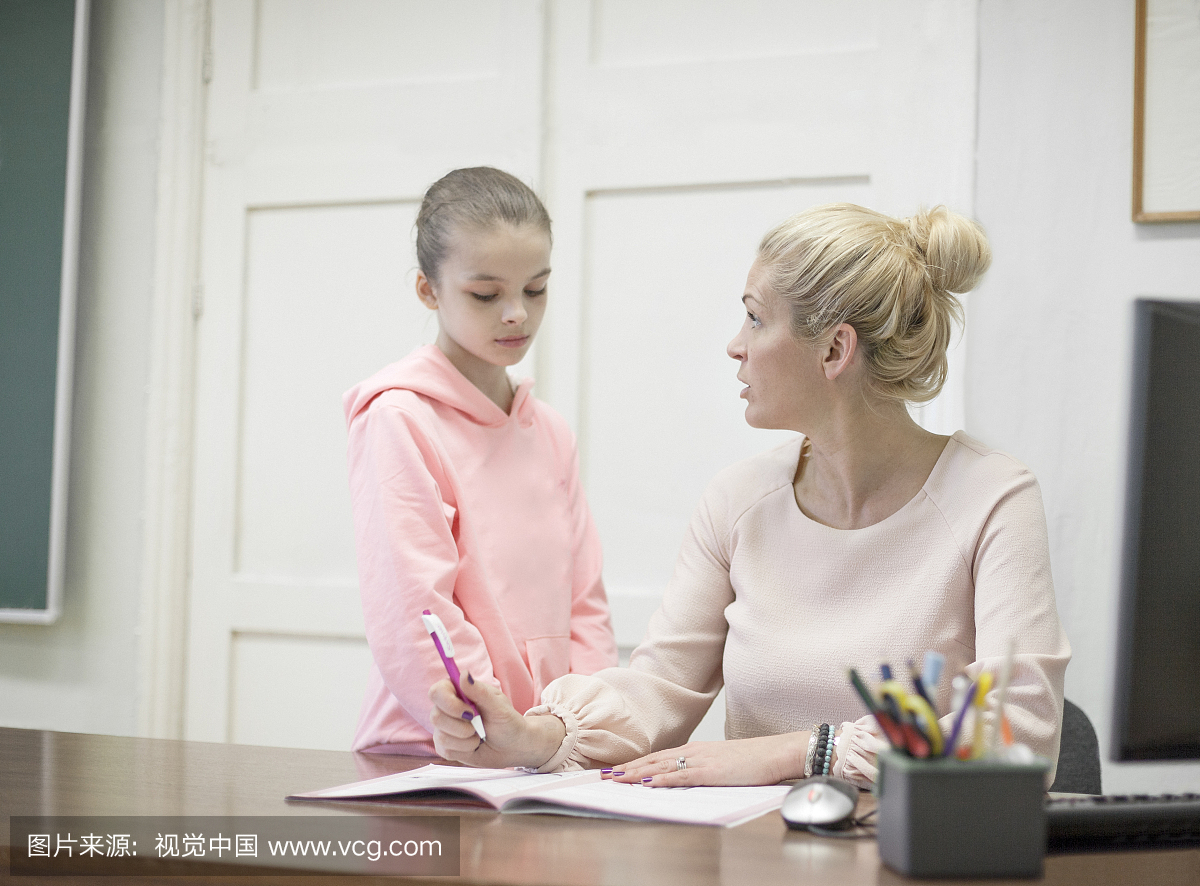 Young pupil at teachers desk with serious teach
