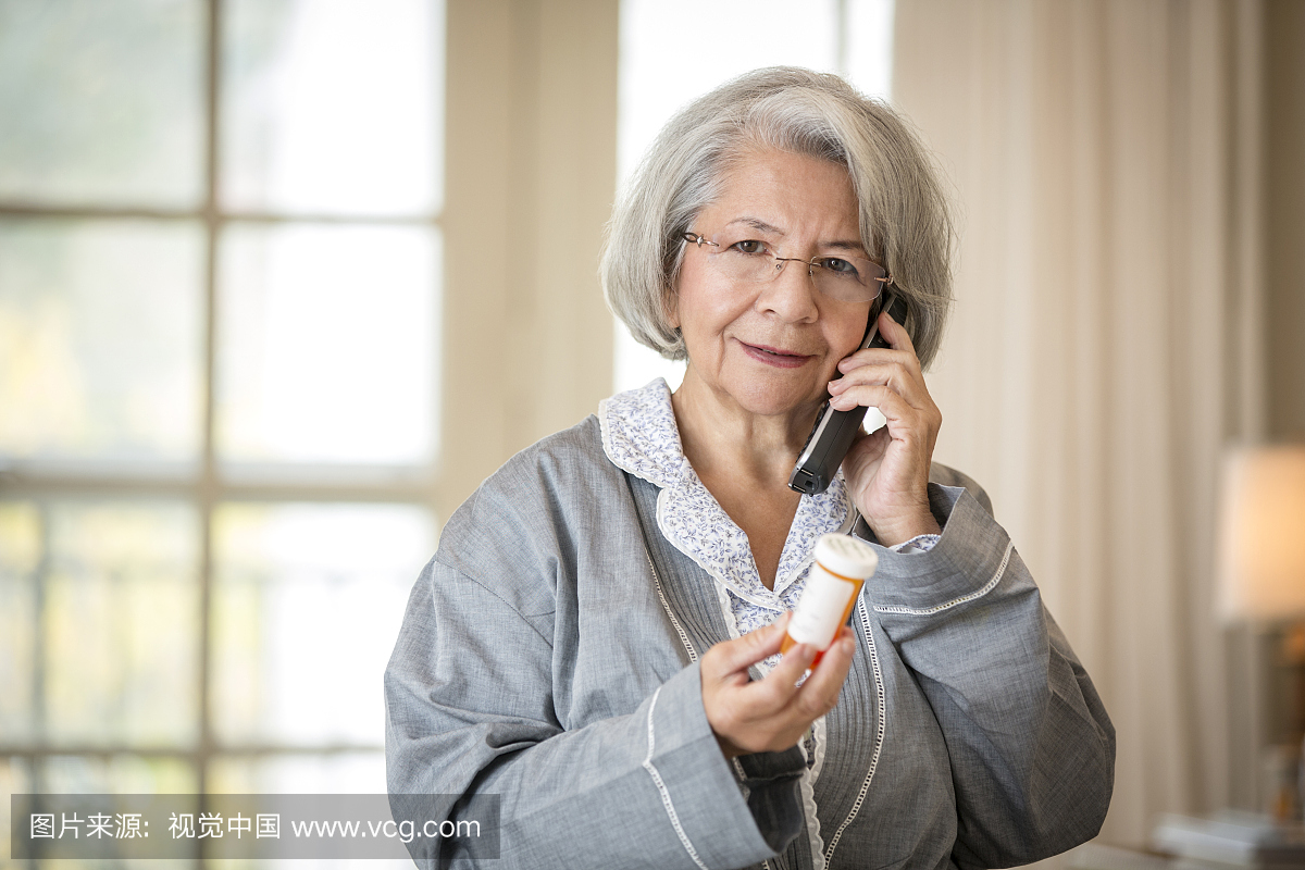 老年人皱眉的西班牙裔妇女使用电话持有药物