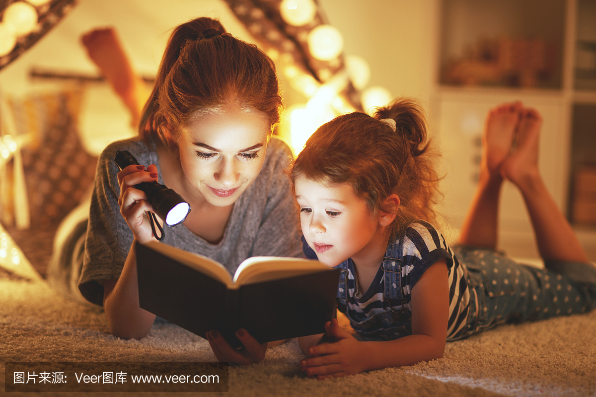 母亲和孩子的女儿在睡觉前读一本书和一个手电