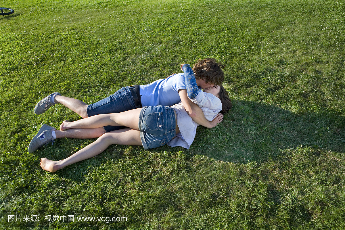 青少年的夫妇躺在草地上,亲吻