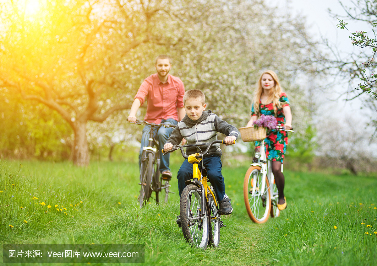 幸福的家庭在春天的花园里骑自行车