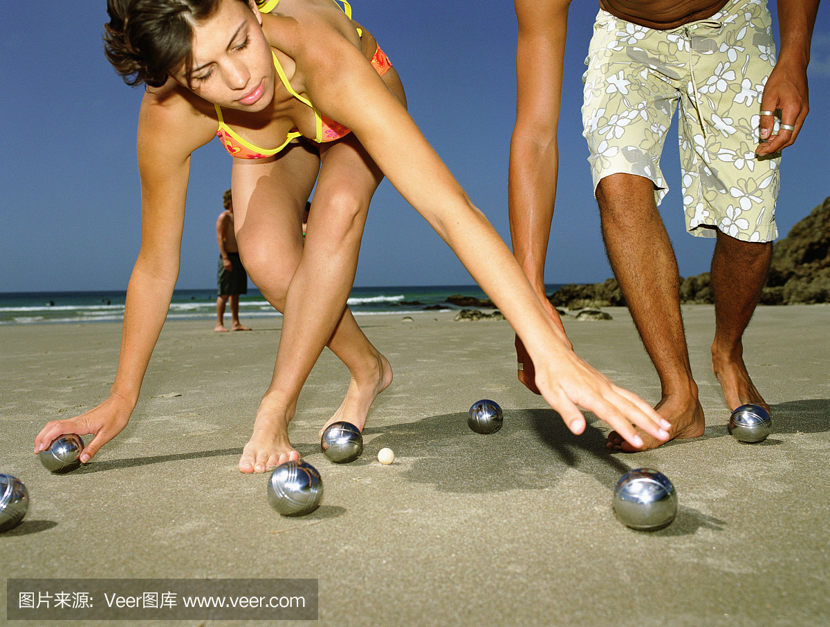 年轻的成年人在海滩上玩滚球,女子捡球