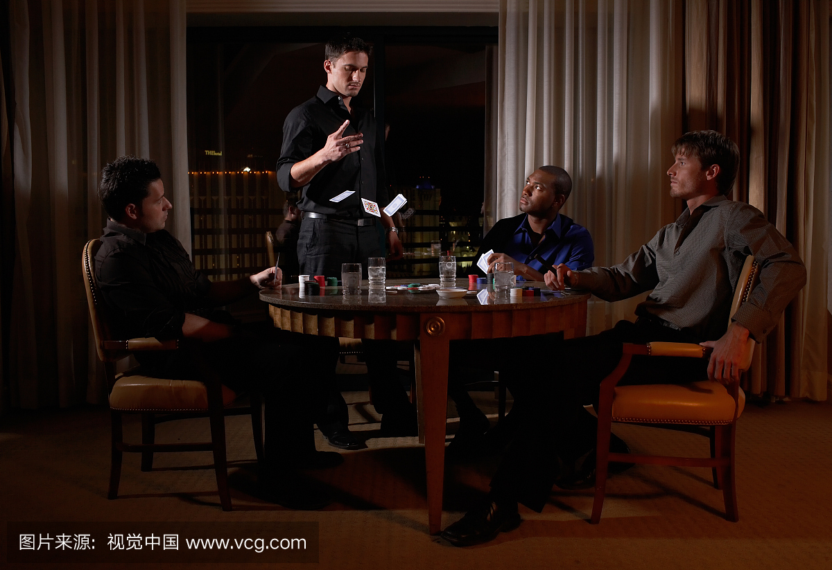 四人坐在圆桌上黑暗的酒店房间玩纸牌,一个人