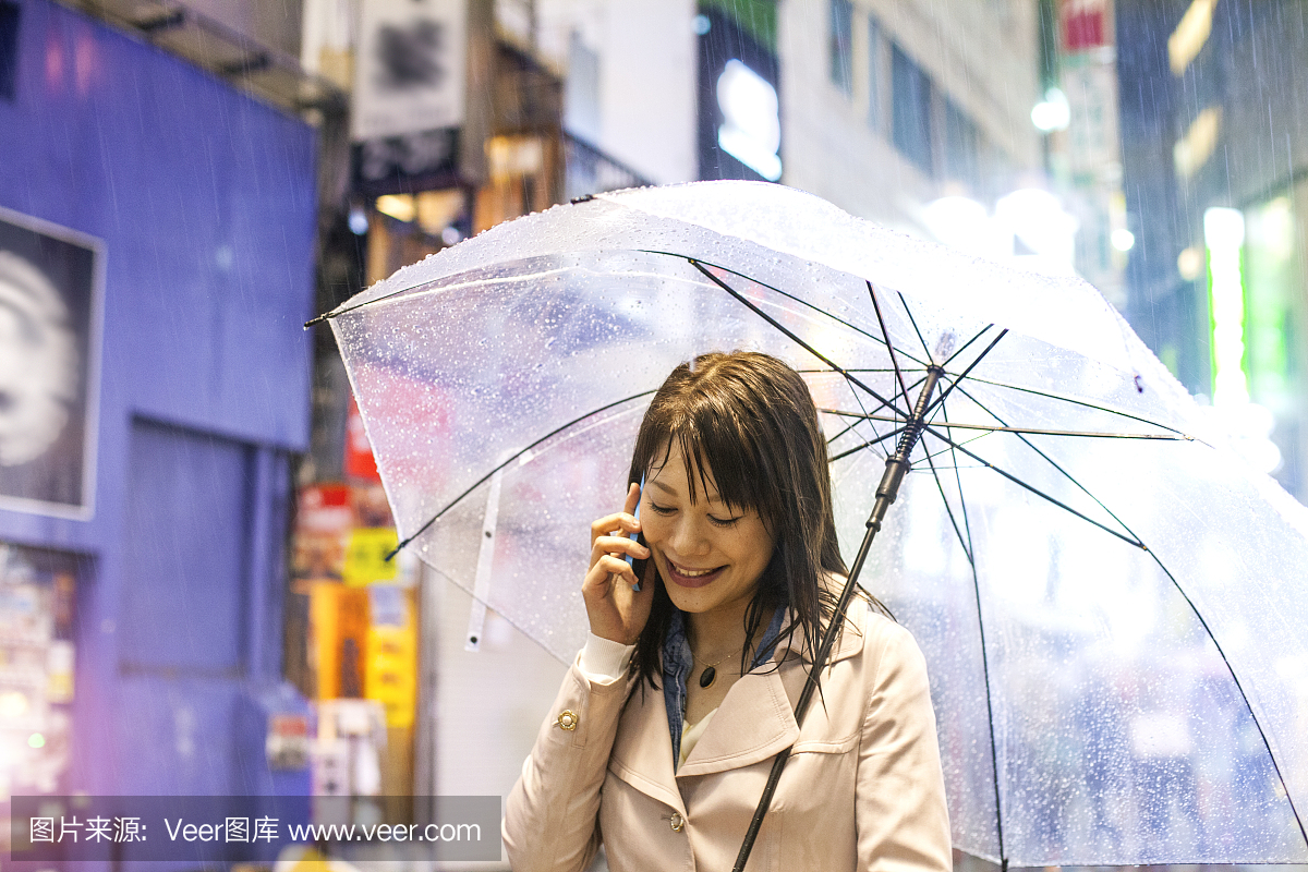 微笑的日本女子与伞在电话在东京