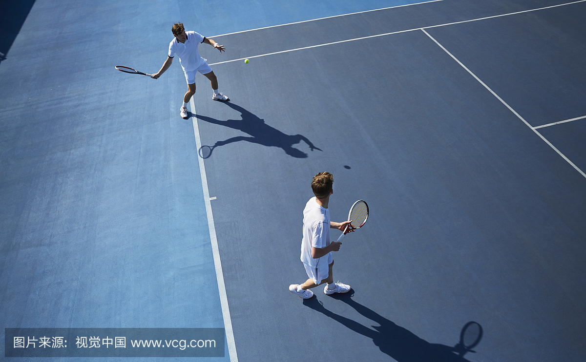 年轻男性双打在晴朗的蓝色网球场上打网球的网