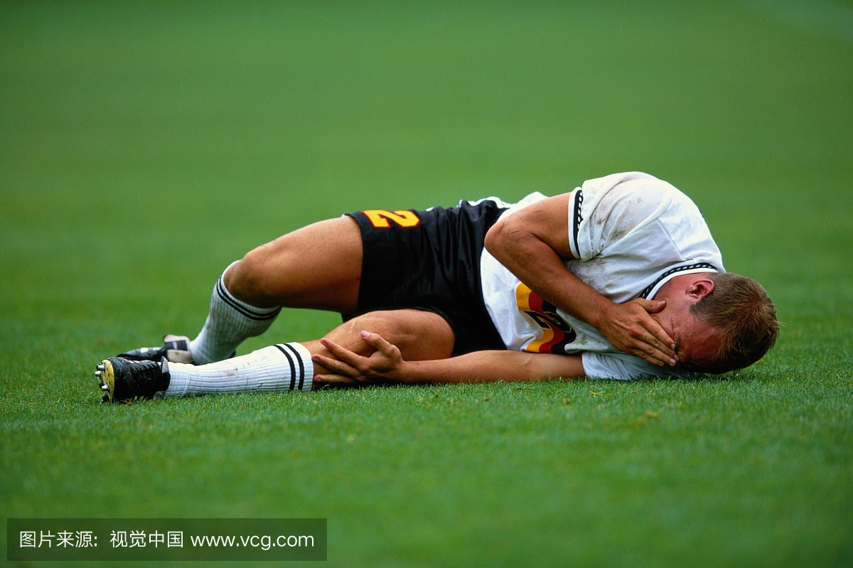 受伤的足球运动员躺在草地上,抱着膝盖