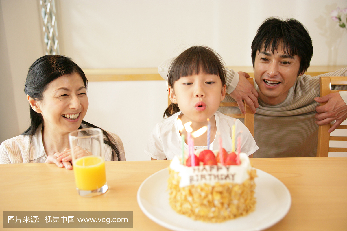 女孩在生日蛋糕上和他们的父母在一起吹蜡烛
