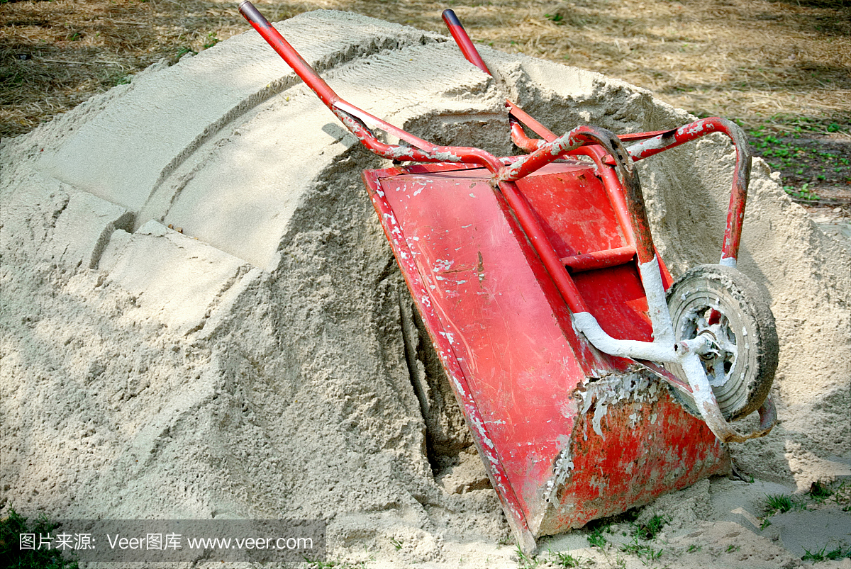 红色的单轮建设车停在一堆沙附近的建筑工地