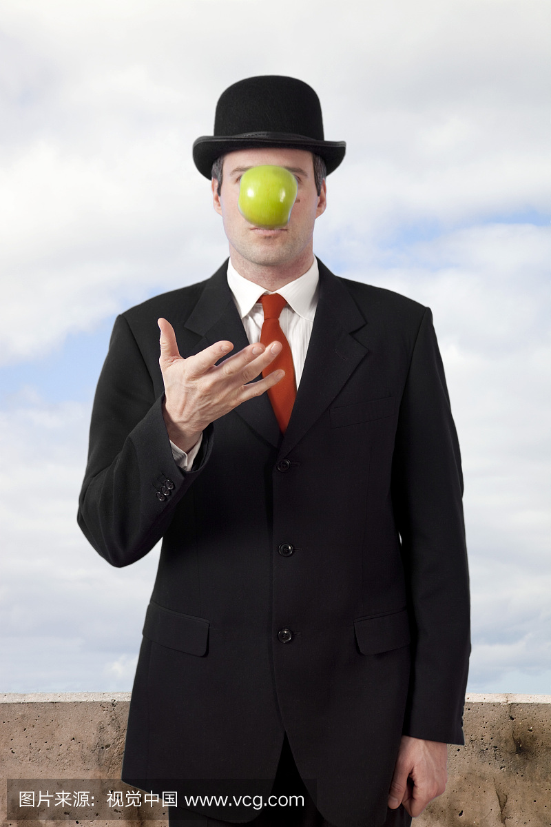 男人在西装和德比帽子把苹果摆在脸前