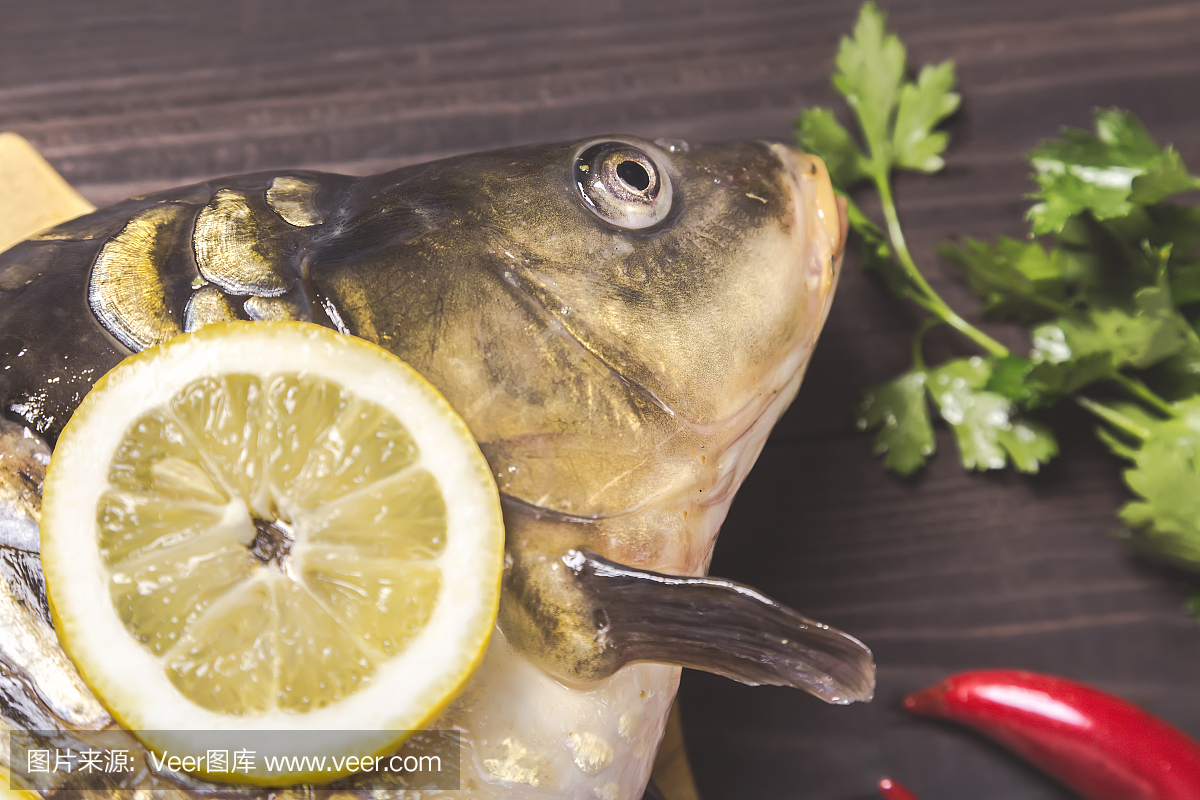 镜子鲤鱼河鱼与柠檬,草药和胡椒在黑木桌上