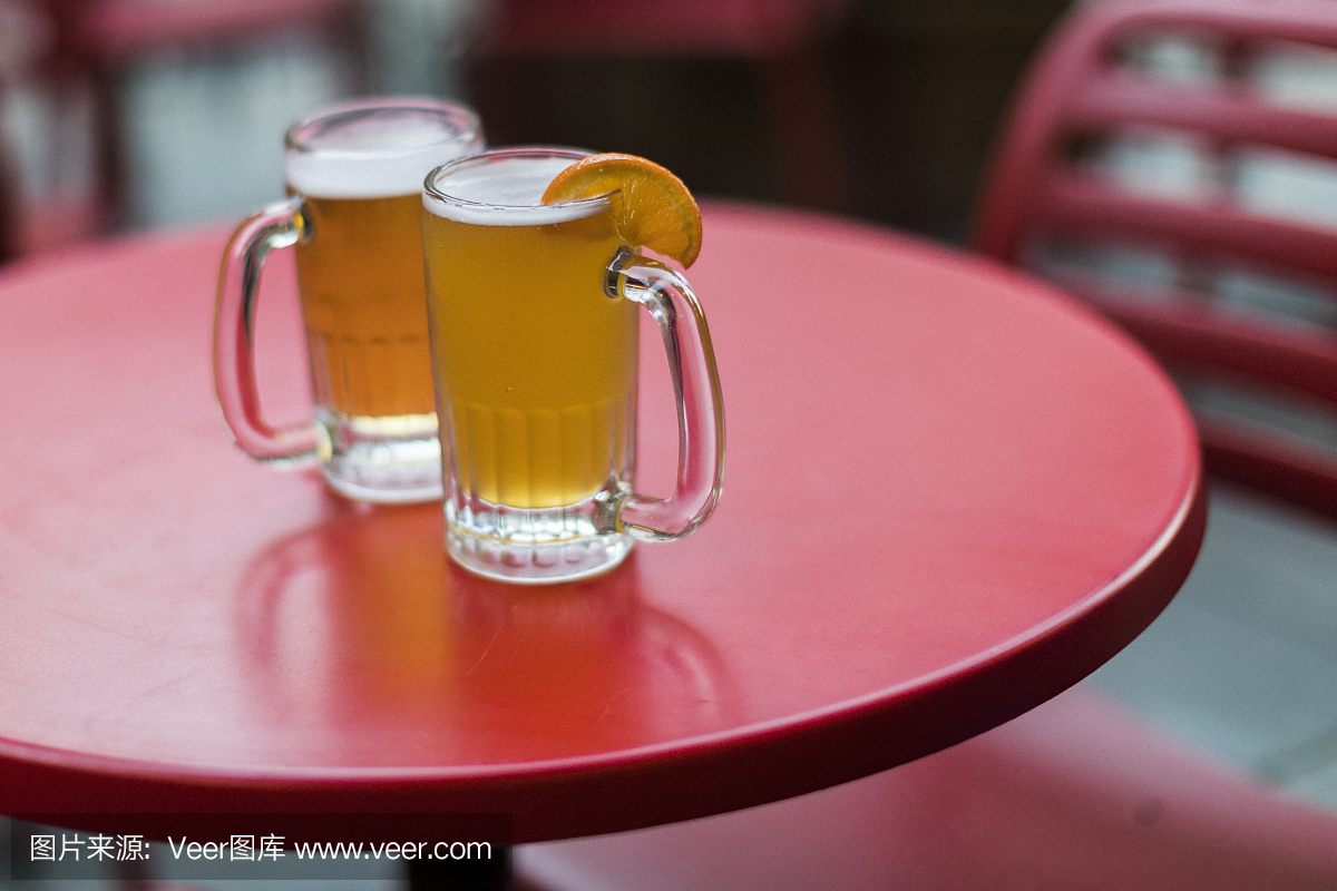 酒吧露台的红桌上的两杯清爽的啤酒杯,一杯是