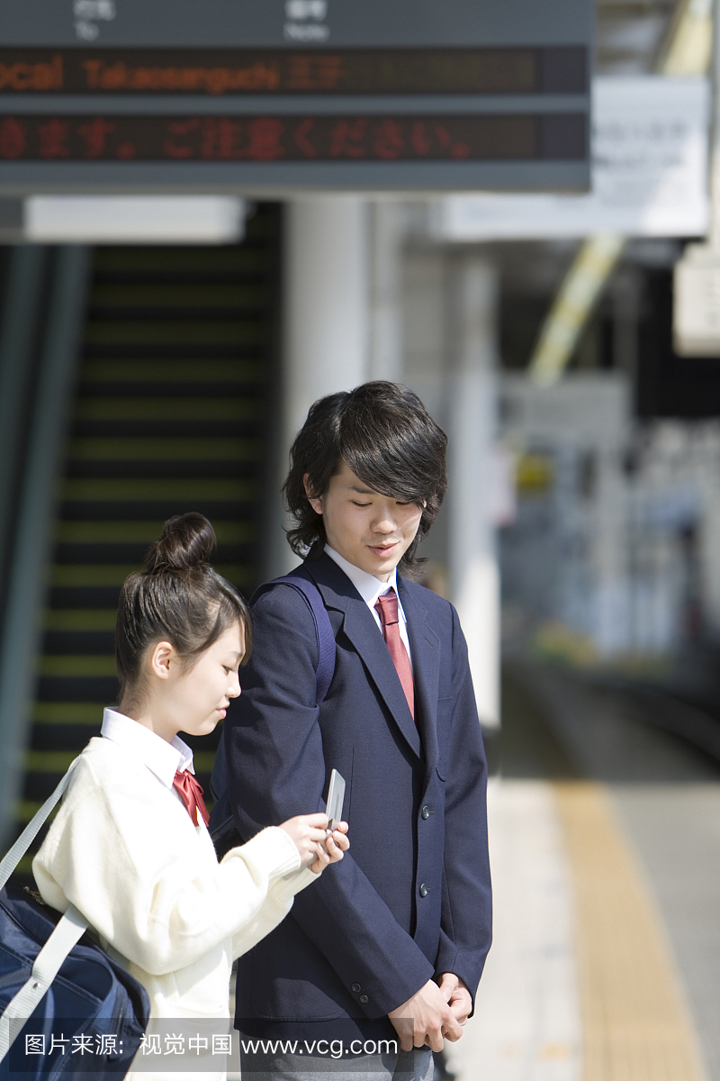 高中生在平台上等着火车,拿着手机的女孩
