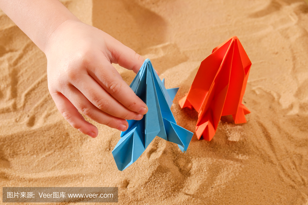 快乐的孩子男孩玩手工折纸纸,火箭在沙滩上,启