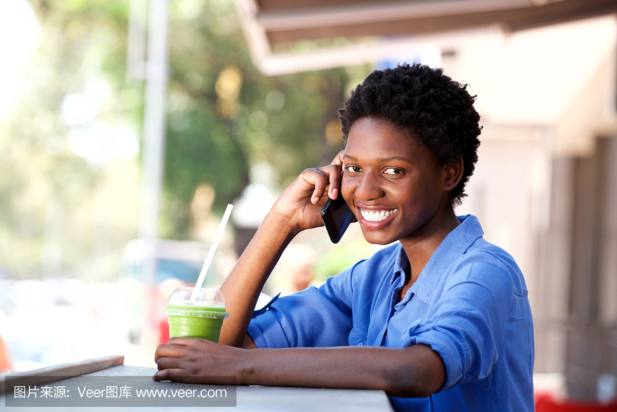 坐在咖啡馆和打电话的微笑的年轻非洲妇女